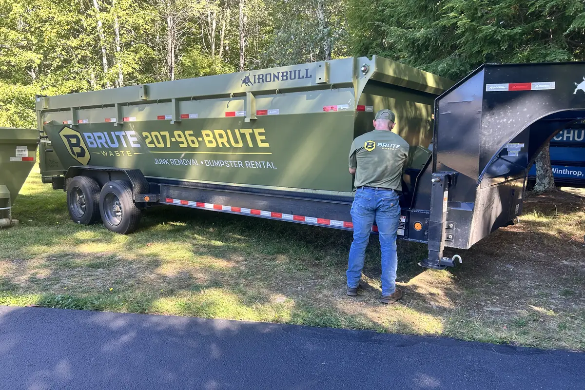A Brute Waste crew member working at the gooseneck hitch of a loaded dumpster trailer