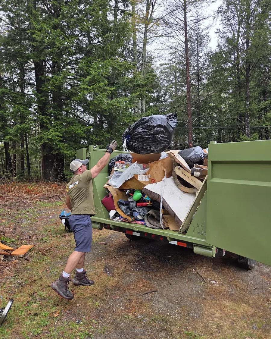 A Brute Waste crew member swinging a full bag up over the side rail of a loaded dumpster