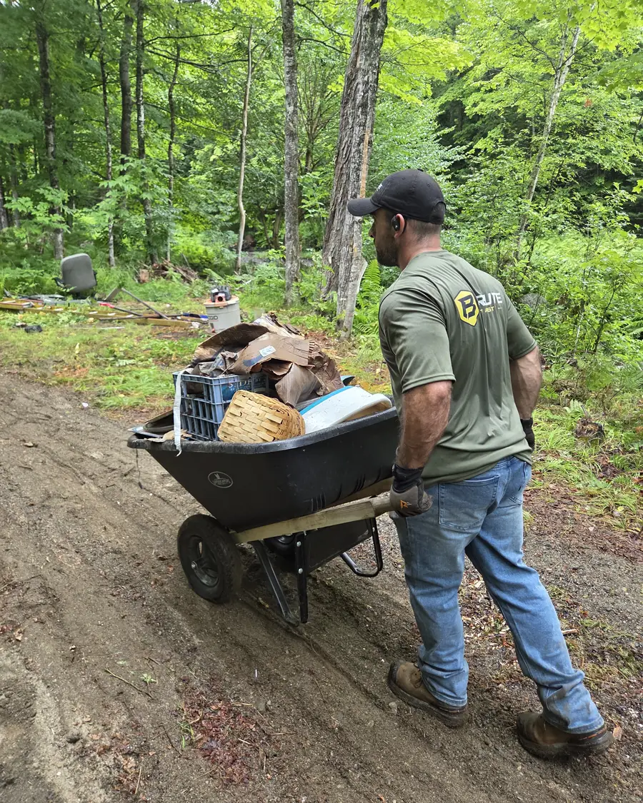 A Brute Waste crew member pushing a wheelbarrow piled with household waste