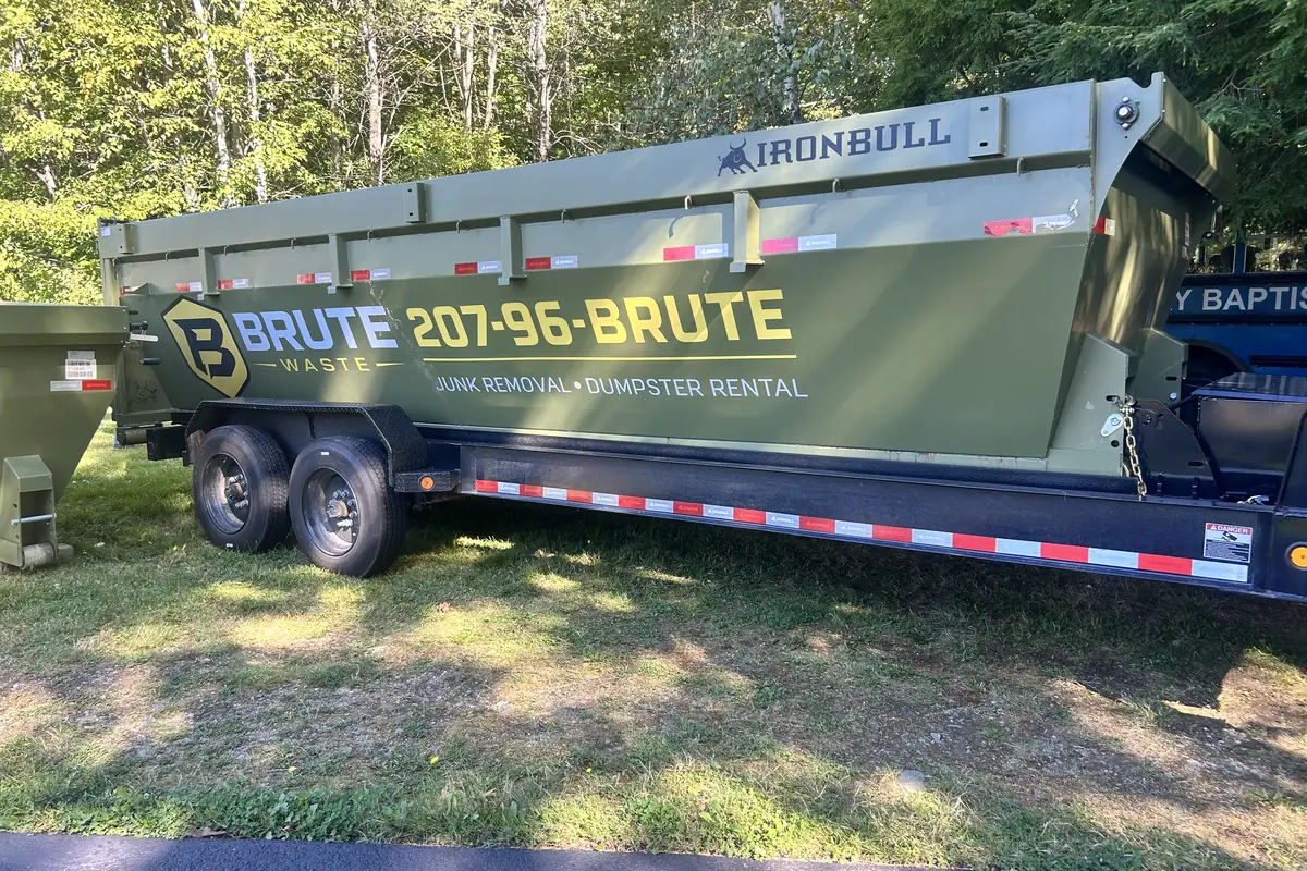 A long Brute Waste dumpster on a trailer parked beside a commercial building