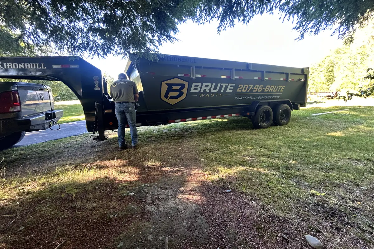 A Brute Waste crew member walking a customer around the dumpster on a shaded driveway