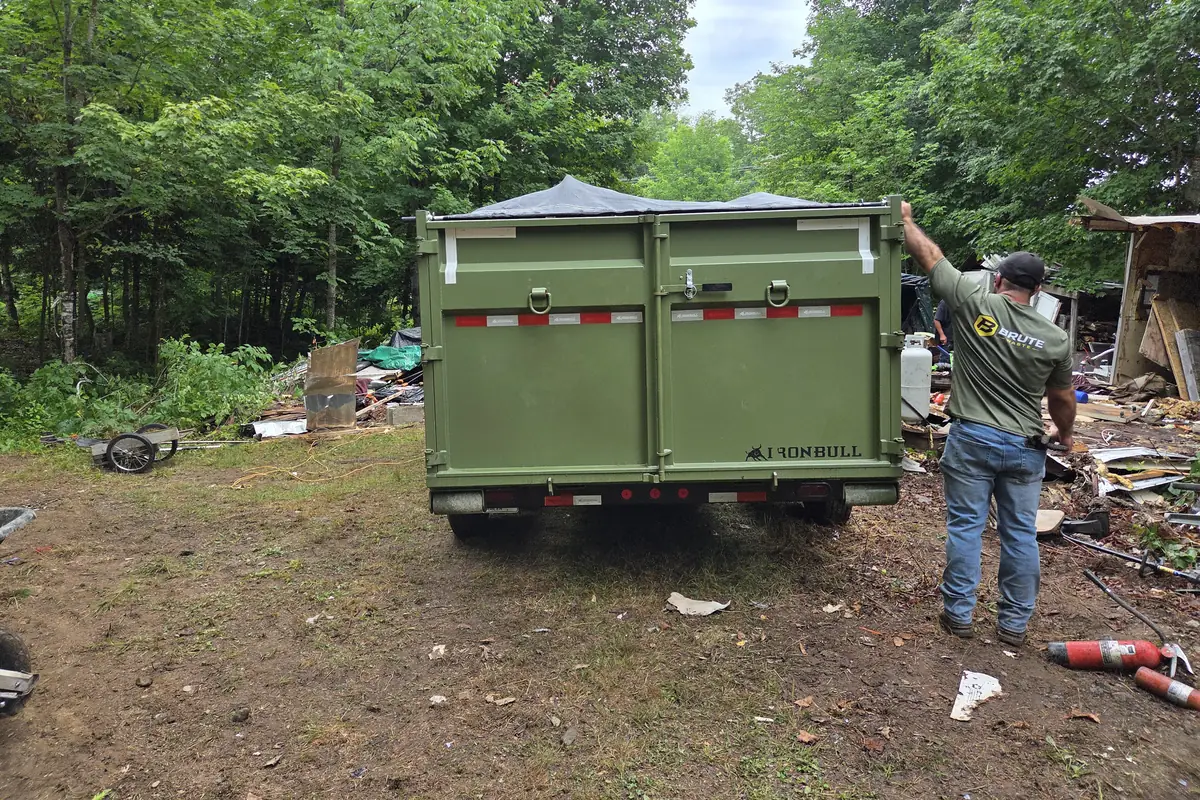 A Brute Waste crew member loading demolition debris onto the back of the trailer at a cleared site