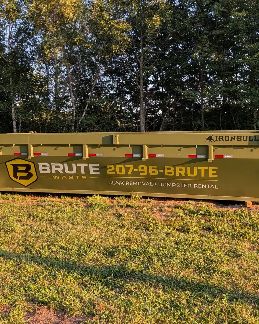A green Brute Waste roll-off dumpster set on a mown lawn in evening light