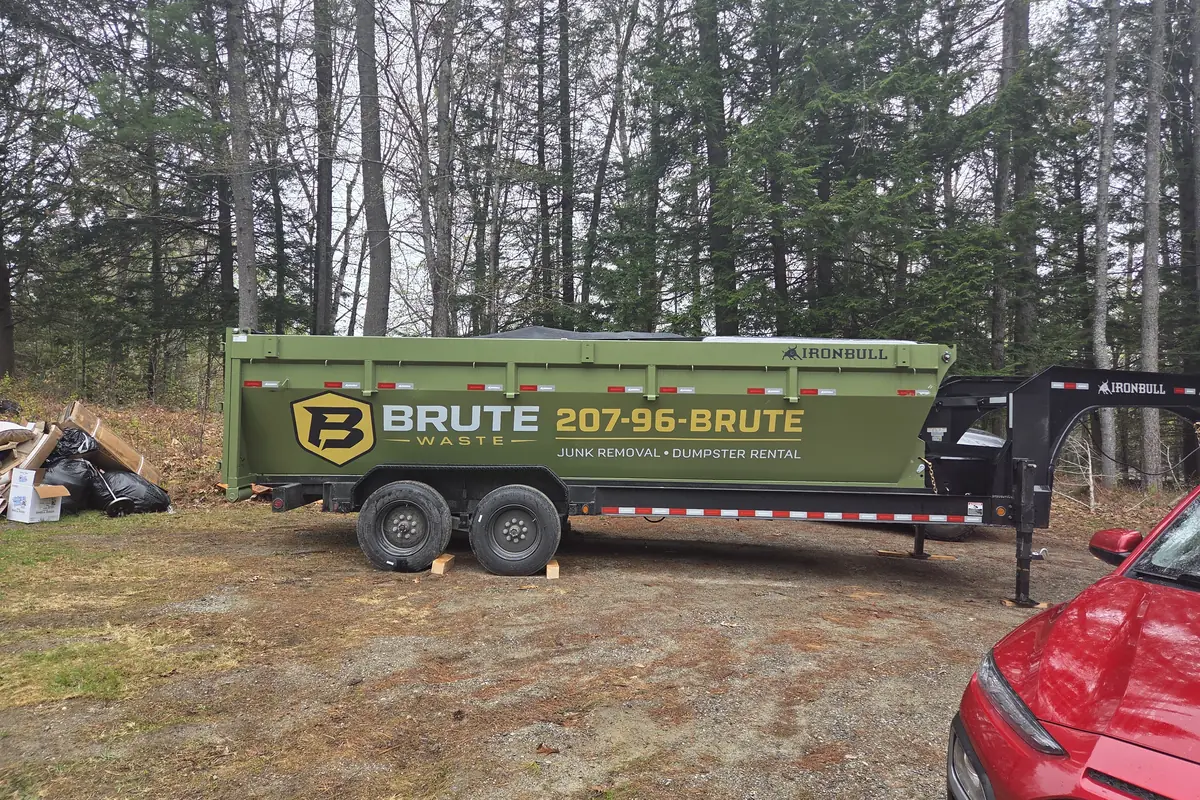 A Brute Waste dumpster on a gooseneck trailer parked on a rural property in evening light