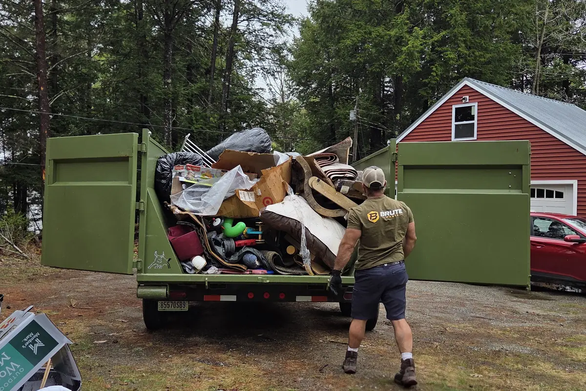 A loaded Brute Waste dumpster beside a red Maine barn at the end of a cleanout