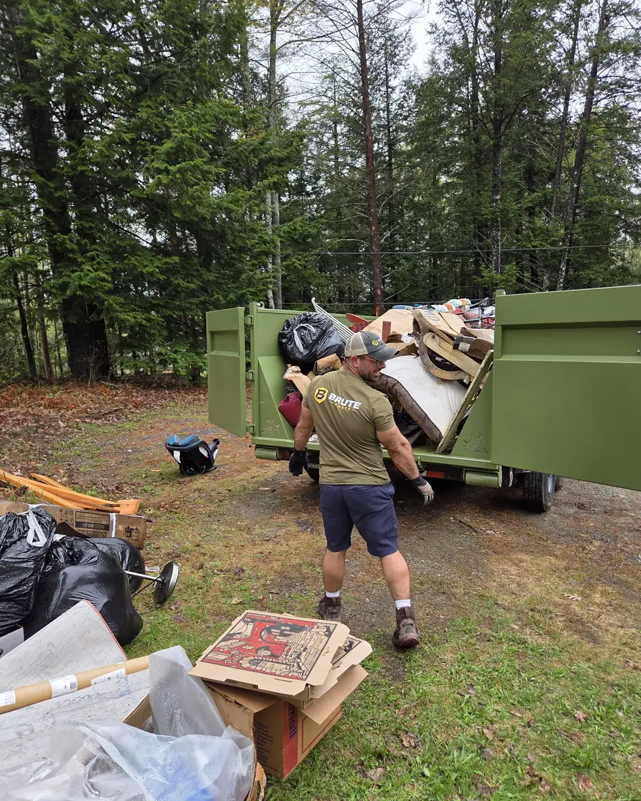 A Brute Waste crew member hand loading household junk over the rail of a dumpster
