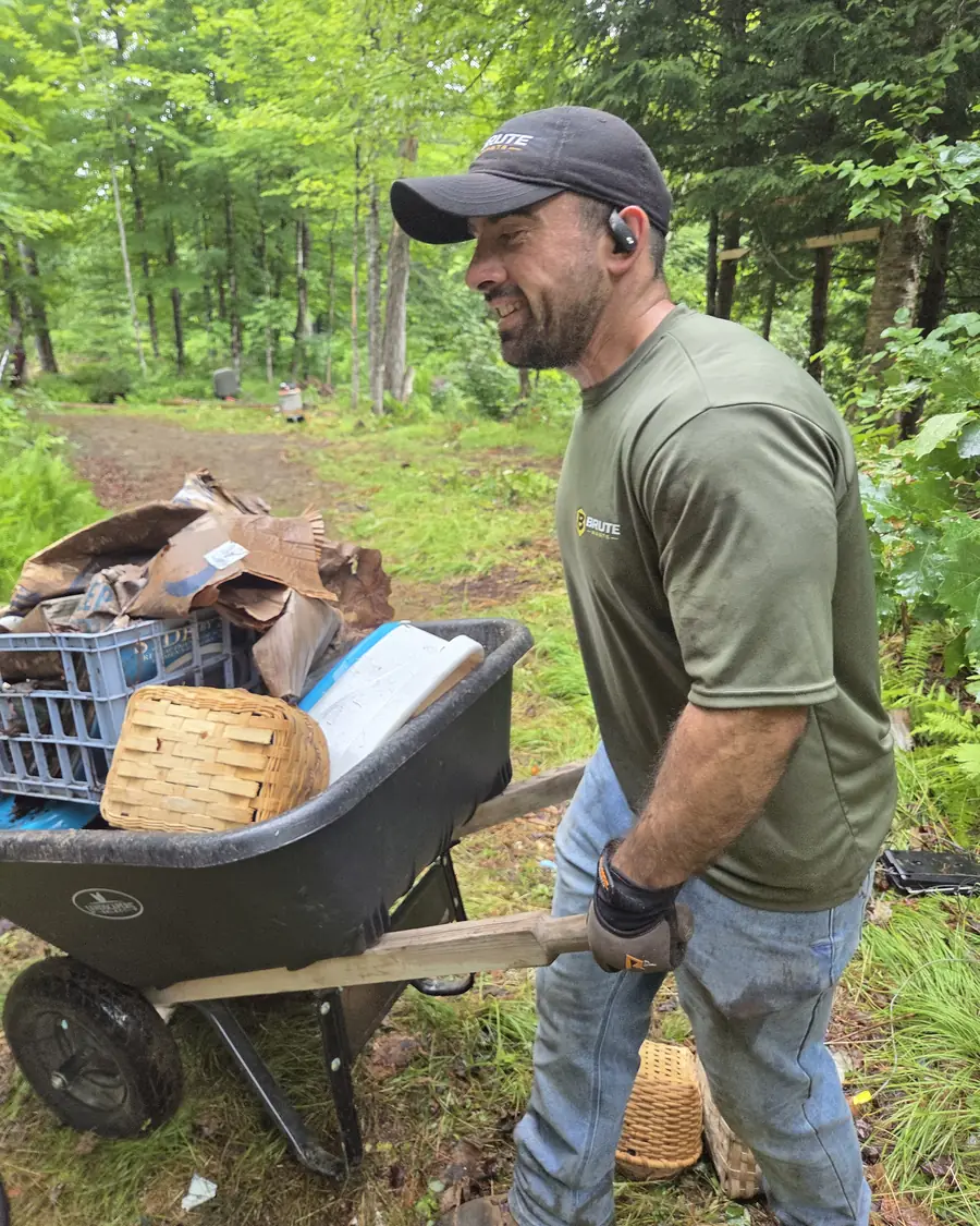 A Brute Waste crew member pushing a loaded wheelbarrow of junk out along a dirt track