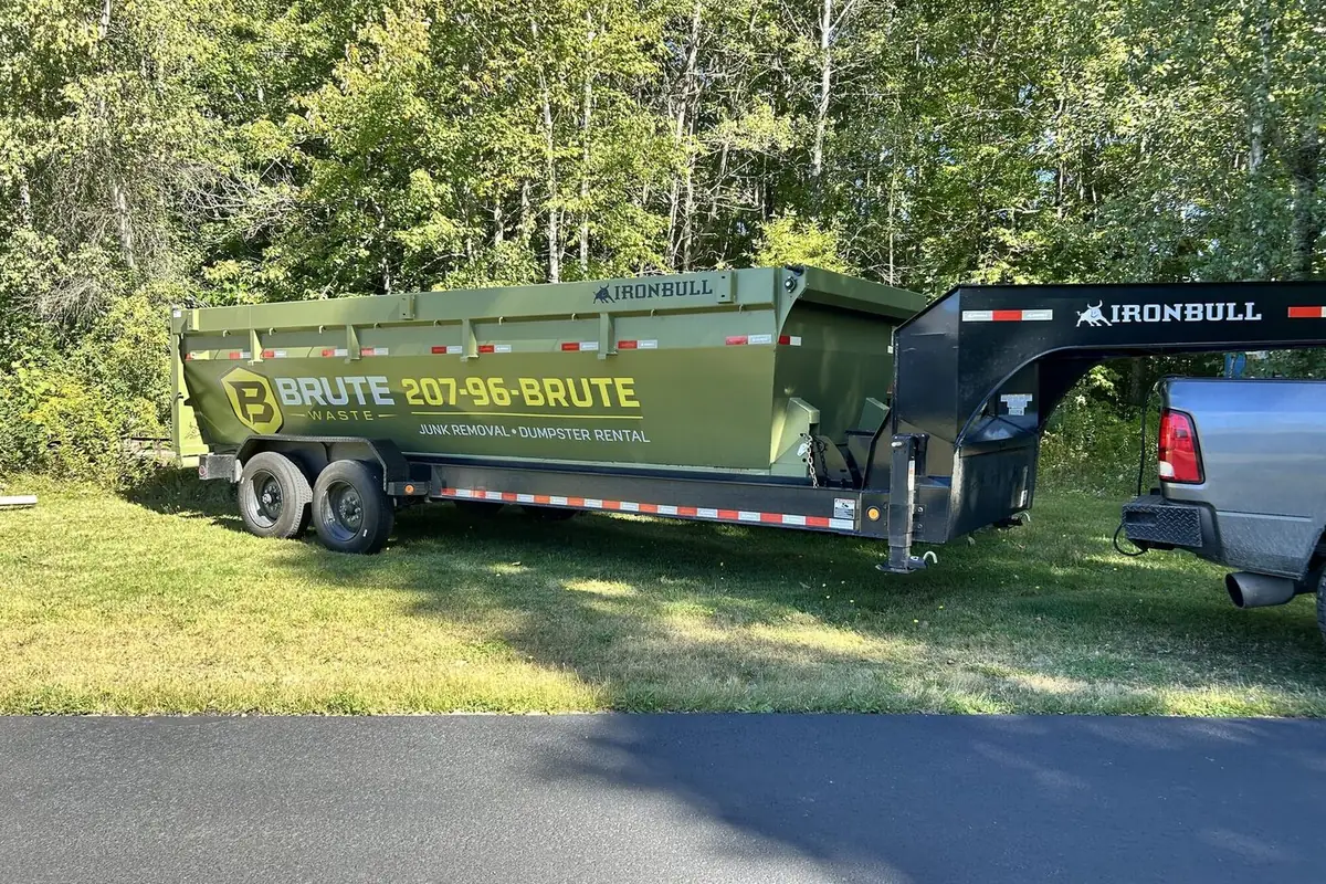 A Brute Waste dumpster on a gooseneck trailer hitched to a pickup on a lawn
