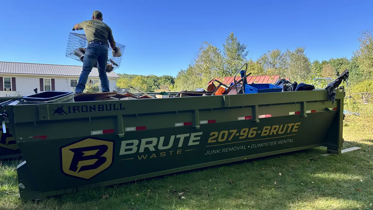A loaded Brute Waste roll-off dumpster against a clear blue Maine sky