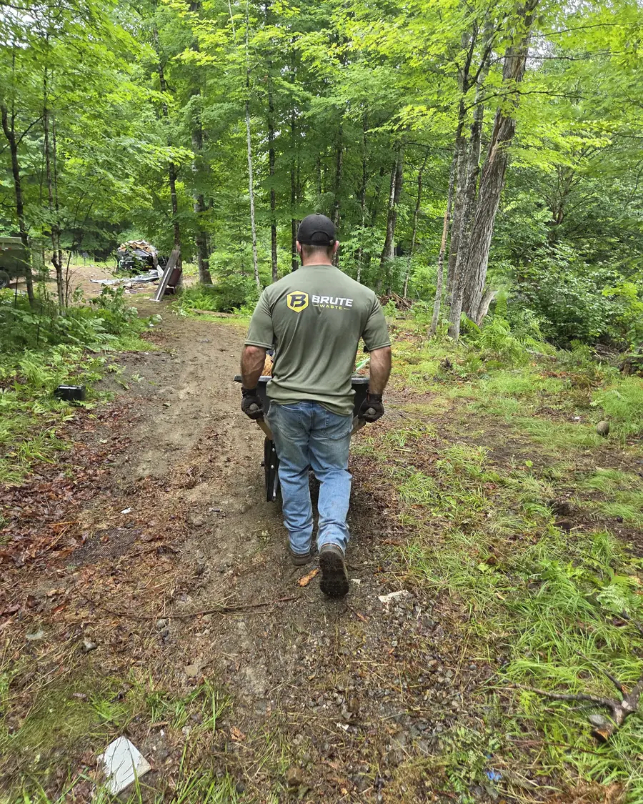 A Brute Waste crew member walking a loaded wheelbarrow down a long wooded track
