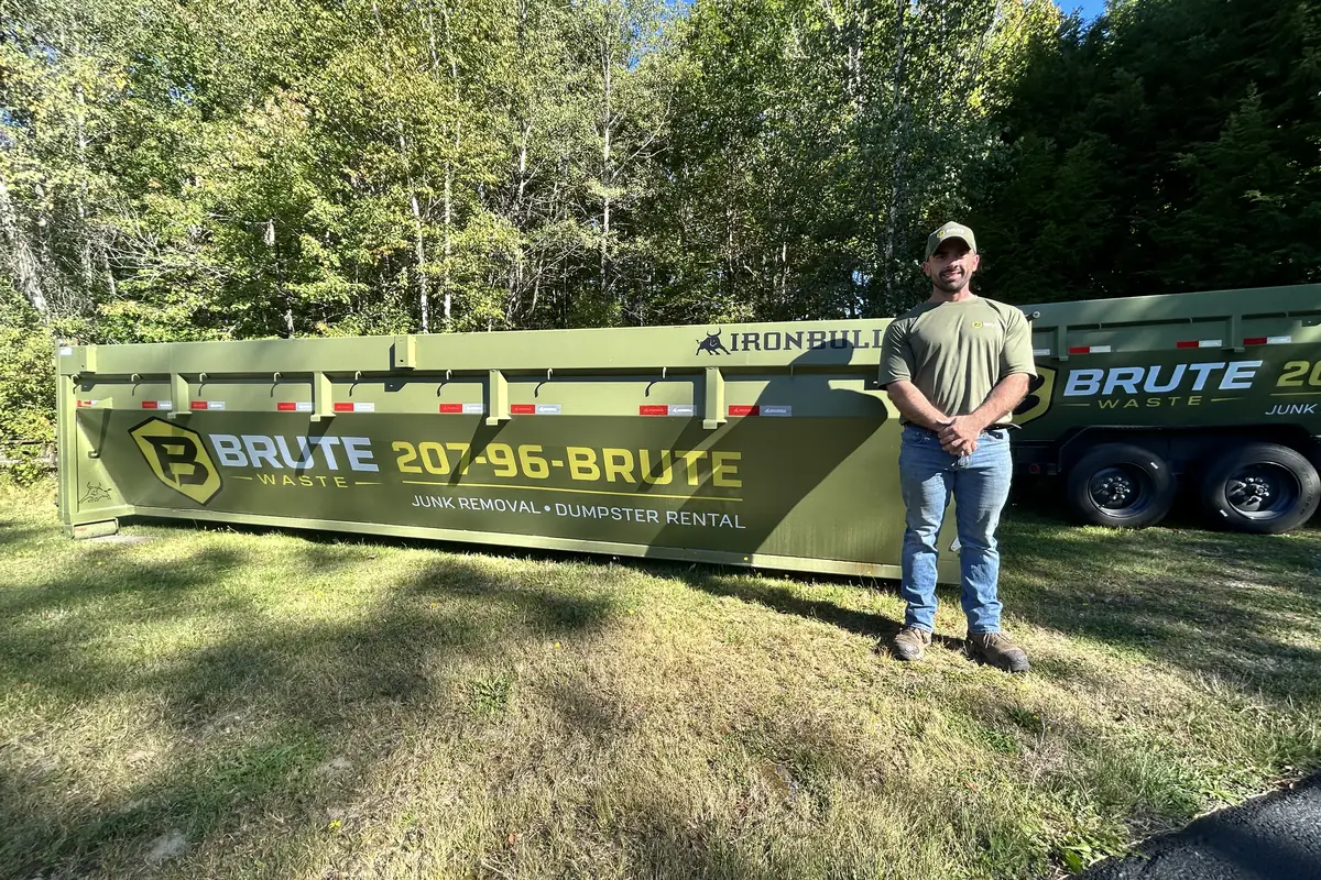A Brute Waste crew member standing beside a roll-off dumpster on a Maine property, ready to start