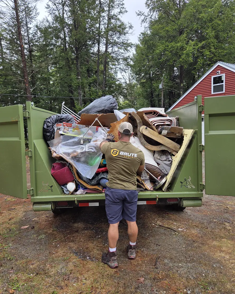 A Brute Waste crew member lifting household waste over the side rail into a loaded dumpster