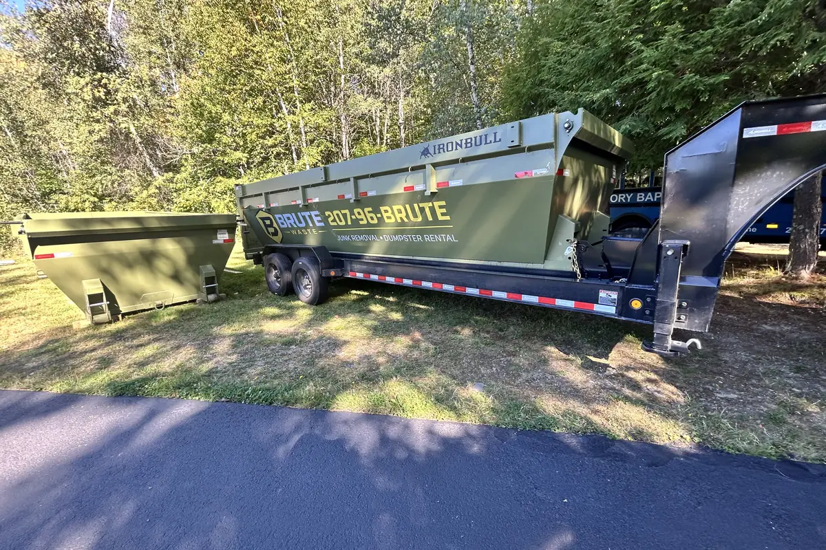 A Brute Waste dumpster tilting off the back of a gooseneck trailer onto a lawn