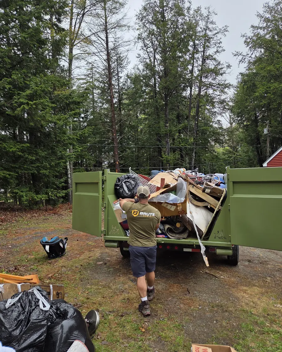 A Brute Waste crew member reaching deep into a loaded dumpster to pack the load down