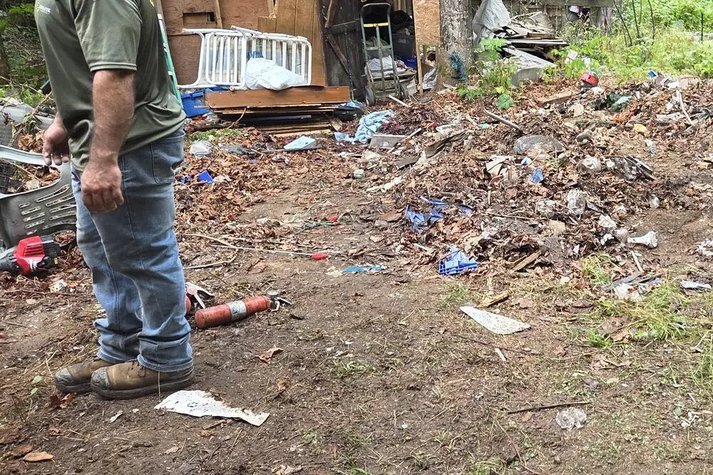 A Brute Waste crew member beside a collapsed plywood shed part way through a teardown