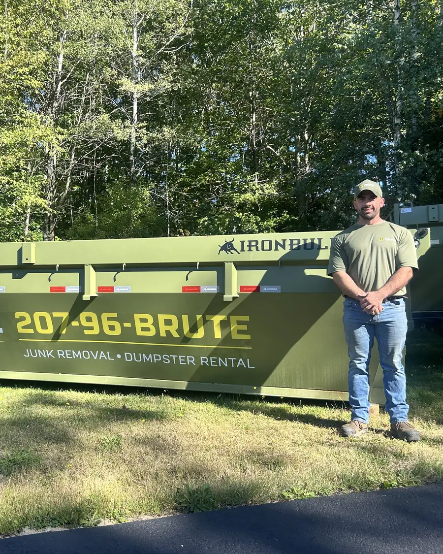 A Brute Waste crew member standing beside a roll-off dumpster on a Maine property