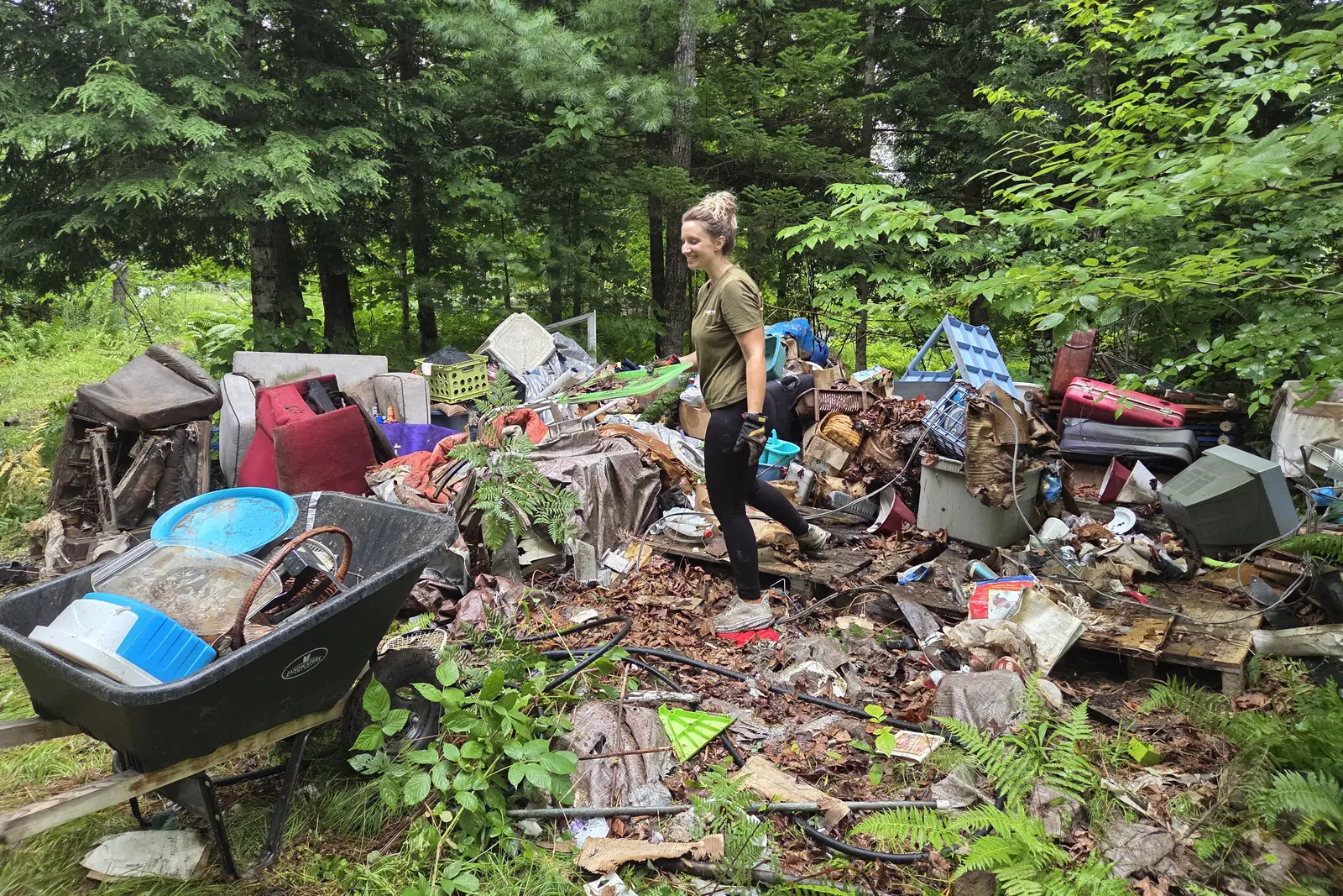 A large pile of dumped household furniture and waste on a wooded Maine property being worked by a Brute Waste crew member