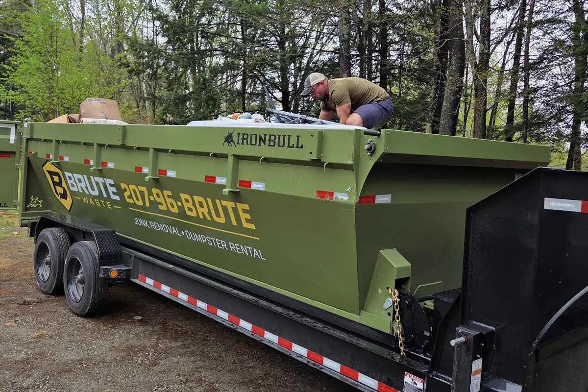 A Brute Waste dumpster trailer side on at a wooded job site part way through a load