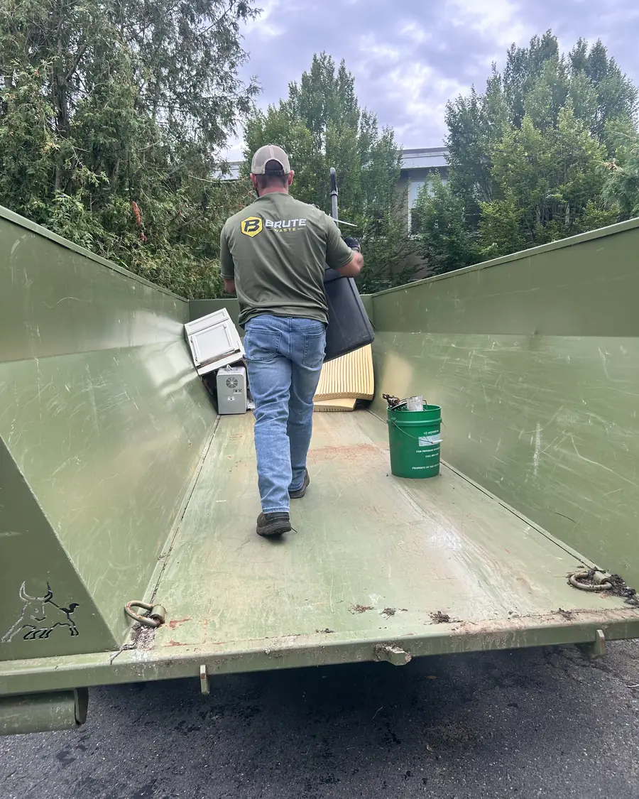 A Brute Waste crew member carrying a tear out load up the ramp into the back of a dumpster