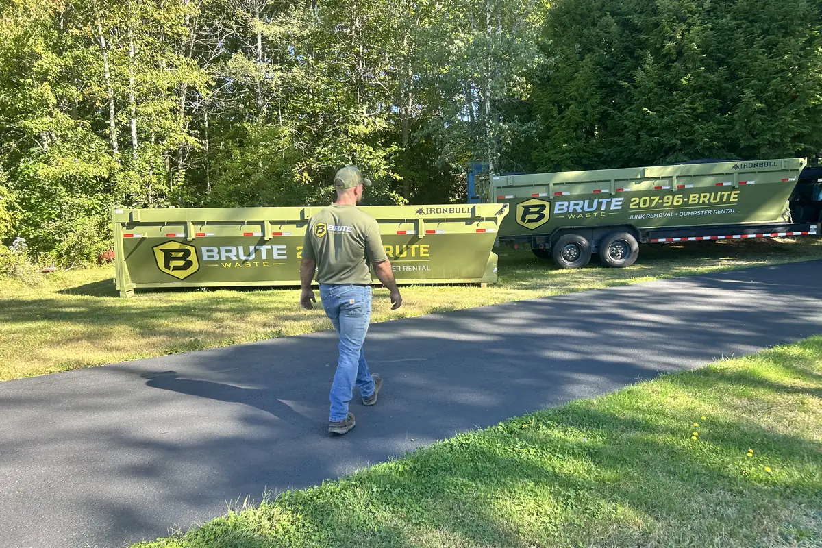 A Brute Waste crew member walking back along a dumpster parked on a residential driveway