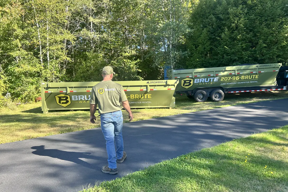 A Brute Waste crew member walking back along a roll-off dumpster parked on a driveway