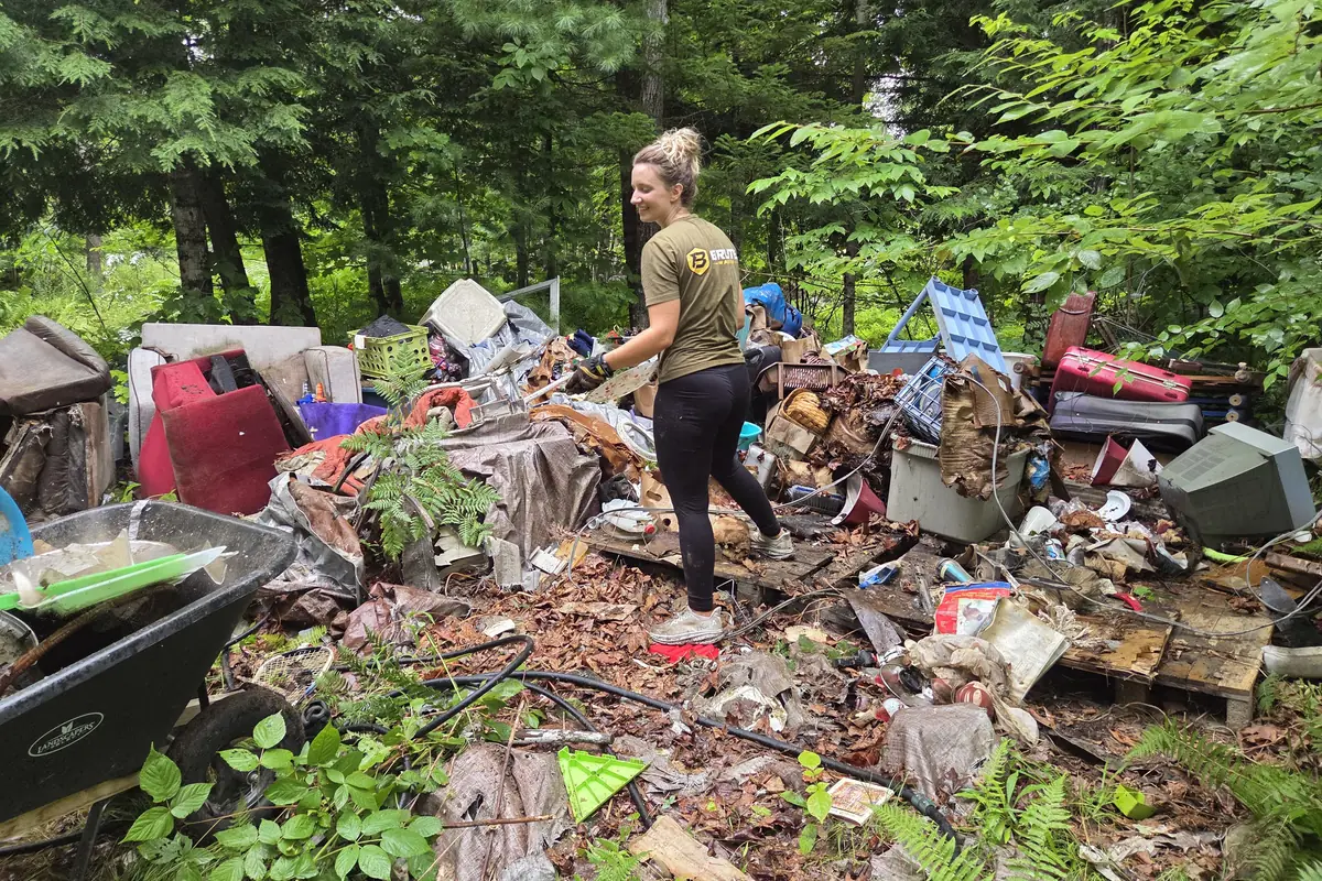 A Brute Waste crew member working through a large pile of dumped household waste on a wooded lot